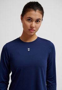 Marineblaue langärmlige Sportshirt aus glattem Stoff, mit Rundhalsausschnitt und drei weißen Schulterstreifen auf der Brust.