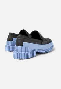 Scarpe slip-on in pelle nera con una robusta suola in gomma blu, dotata di scanalature e finitura testurizzata, progettate per offrire aderenza e comfort.