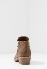 Botte synthétique marron à la cheville avec un motif texturé de serpent, talon effilé et détail de fermeture éclair latérale. Finition intérieure lisse.