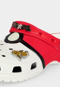 Sabot blanc et rouge avec des trous de ventilation, un motif noir et blanc près de l’orteil, et un petit pendentif Pokémon Eevee sur le dessus.