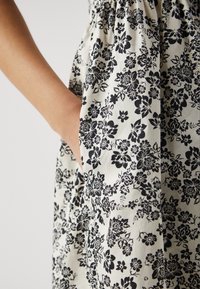 Květinové šaty v černobílé bavlně s nařasenými detaily, vyznačující se kapsou a propracovanými květinovými potisky na látce.