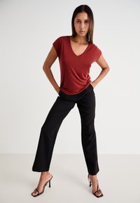 Rood v-hals t-shirt met korte mouwen, gecombineerd met zwarte rechtpijpenbroeken en zwarte open teen hakken, staand gepositioneerd.