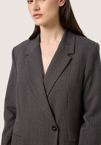 Grå pinstribet blazer med sømfald, enkelt knaplukning og forlommes detaljer; tekstureret stof med en skræddersyet pasform.