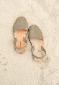 Pair of olive green open-back sandals with tan insoles resting on light sandy beach surface