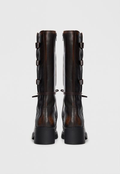 Brown leather knee-high boots with a smooth texture, featuring a zip closure, multiple buckles, and a sturdy block heel.