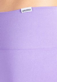 Lila Leggings mit einem gerippten Bund und einer glatten Textur, ausgestattet mit einem kleinen Etikett mit dem Markennamen "SMILODOX" oben.