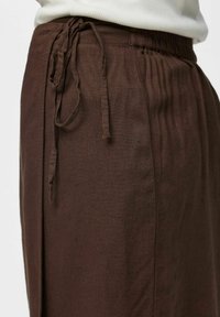Pantalon en lin marron avec taille élastique et cordon noué, porté avec un haut clair rentré.