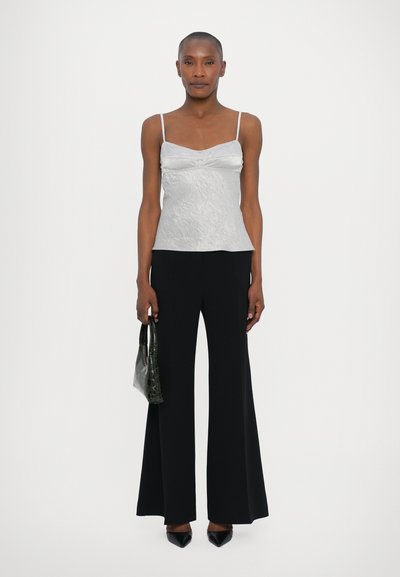 Camiseta de satén plateada con un acabado texturizado, combinada con pantalones negros de pierna ancha y tacones negros de punta. Sosteniendo un pequeño bolso verde.