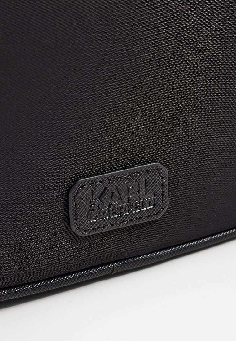 Primer plano de una tela negra texturizada con un parche rectangular cosido y embellecido con el logo "KARL LAGERFELD".