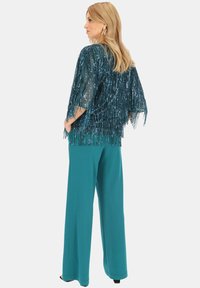 Turkusowa bluzka z frędzlami i cekinowymi detalami oraz szerokie spodnie w pasującym turkusowym kolorze. Teksturowana tkanina zwiększa wizualne zainteresowanie i styl.