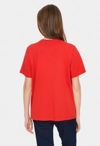 Tricou roșu cu mânecă scurtă, din bumbac, cu gât rotund și o croială lejeră. Văzut din spate, cu o textură netedă.