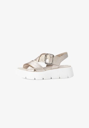 Sandales métalliques dorées avec un design à bandes croisées et une large semelle blanche. Équipées d'une boucle carrée argentée en accent sur la sangle de cheville.