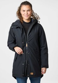 Parka noire avec fermeture éclair et pression, capuche, deux poches avant et doublure intérieure texturée. Présente un petit écusson logo.