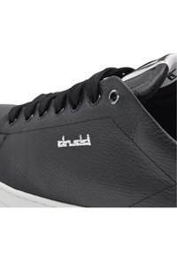 Black leather sneaker with textured surface, white logo on the side, and black laces. Features metal eyelet and white rubber sole.