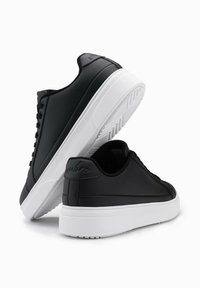 Baskets noires en matériau synthétique lisse avec semelles en caoutchouc blanches, présentant un design minimaliste et un détail de logo subtil au talon.