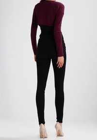 Černé elastické úzké džíny ve střihu na tělo spojené s krátkým burgundským svetrem s dlouhým rukávem. Modelka má na sobě tělové lodičky na vysokém podpatku.