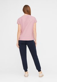Rosa Baumwoll-T-Shirt mit kurzen Ärmeln, kombiniert mit marineblauen Jogginghosen. Die Jogginghosen haben elastische Bündchen und eine glatte Textur. Die Schuhe sind beige.