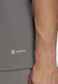 Gray athletic shirt with a smooth texture, featuring a small white "AEROREADY" logo near the hem. Close-up on arm shows natural skin tone.