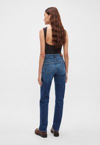 Aukšto liemens mėlyni džinsai vidutinio dzinso, tiesios kojų linijos, su kišenėmis gale ir odiniu lipduku ant juosmens. Lygios tekstūros.