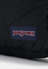 Fekete szövet hátizsák, amelyen egy téglalap alakú kék folt található, rajta a "JANSPORT" felirat fehér és bordó színben hímzve. Tapintásra kellemes felület és tartós kialakítás jellemzi.
