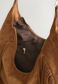 Sac à main en daim marron avec fermeture éclair dorée partiellement ouverte, montrant l'intérieur en tissu foncé et une petite poche intérieure zippée.