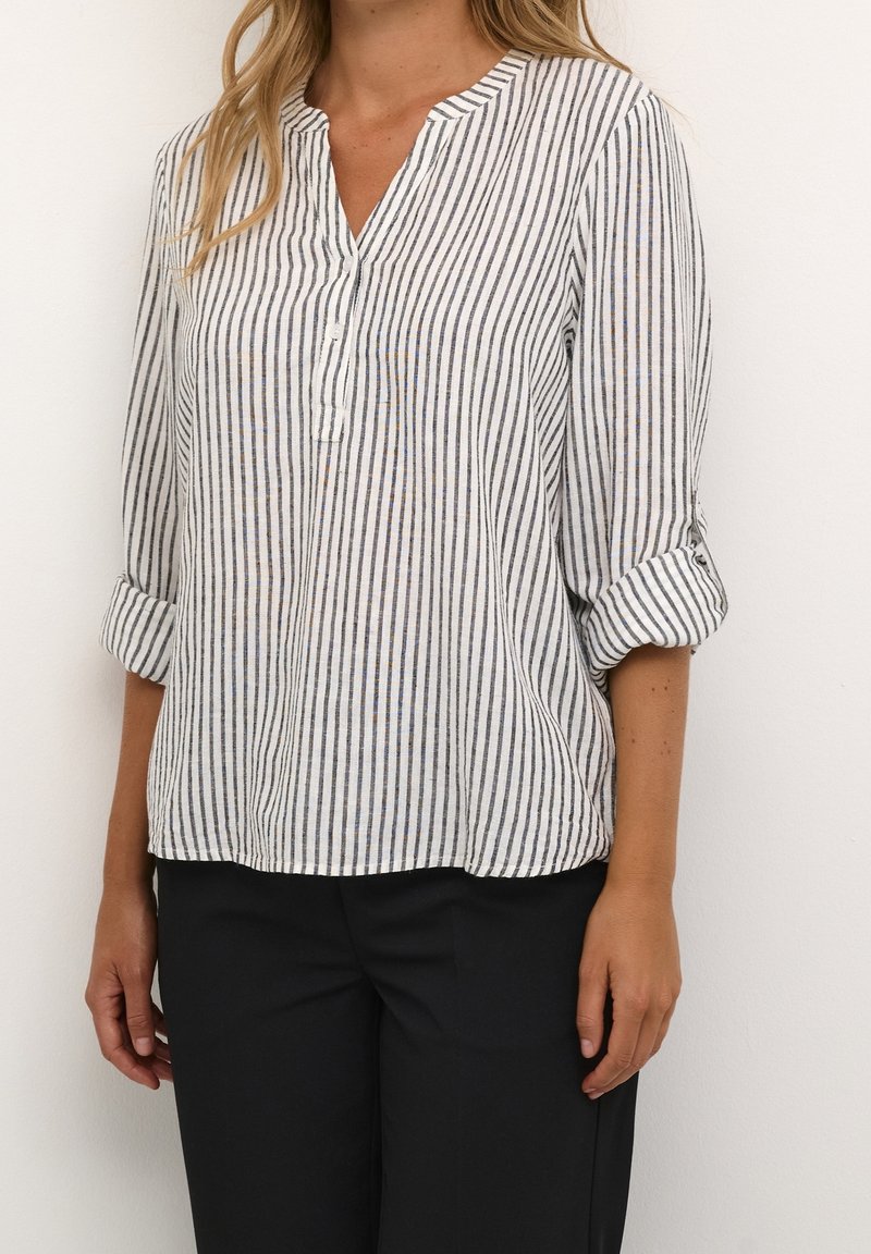 Blusa leggera a righe con scollatura a V e maniche arrotolate; presenta righe blu e marroni su uno sfondo bianco. Tessuto morbido, vestibilità rilassata.