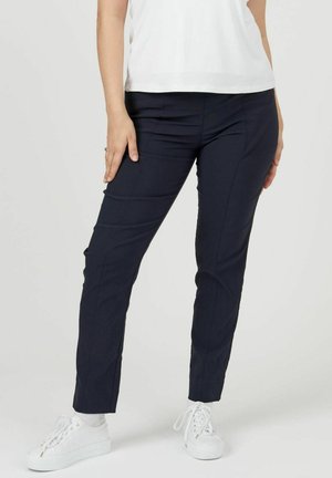 Navyblauwe slim-fit broek van een gladde stof; heeft voorste naden en een strakke vormgeving, gecombineerd met witte sneakers.
