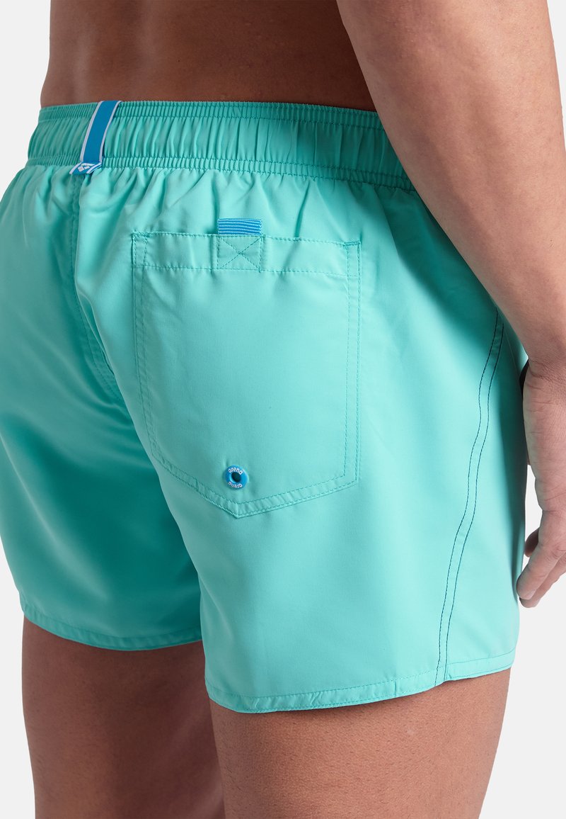 Turkusowe kąpielówki z elastycznym pasem, z tylną kieszenią z niebieskim guzikiem i kontrastowymi detalami przeszyć. Krótki krój.