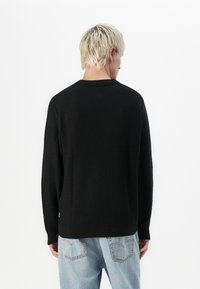 Pull en tricot noir avec un motif texturé, manches longues, col rond et poignets côtelés, vu de dos. Design décontracté.