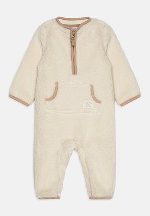 Crèmekleurig fleece babyoveral met lange mouwen, ritssluiting aan de voorkant, bruine bies en een zakje aan de voorkant met een klein label.