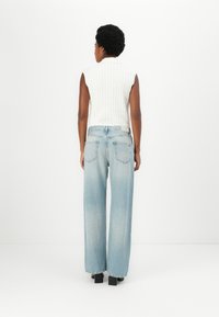 Top sin mangas de punto de cable blanco combinado con jeans de pierna ancha azul claro, que cuentan con un corte recto y bolsillos traseros. Zapatos negros de tacón bloque.