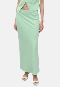 Jupe midi ajustée vert clair avec une texture lisse et un éclat subtil. Elle présente une taille haute et une fente sur le côté pour faciliter le mouvement.