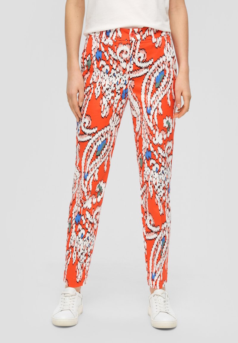 Pantalons rouges à motifs avec des designs en paisley blancs, bleus et verts, coupe slim, taille élastique et longueur jusqu'à la cheville, associés à des baskets blanches.