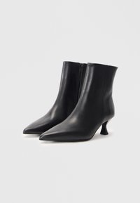 Bottines en cuir noir avec un bout pointu et un petit talon en kitten. Texture lisse avec un subtil éclat et une fermeture éclair sur le côté.