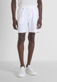 Shorts en lin blanc avec taille élastique et cordon de serrage. Texture lisse et plis sur les côtés. Associés à des baskets blanches.