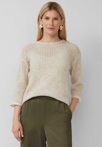 Maglione beige in pizzo con maniche a tre quarti e una vestibilità rilassata; caratterizzato da un motivo aperto. Indossato con pantaloni verde oliva.