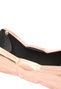 Rosa guldbag med en båtdesign; glänsande yta, svart tygfoder och en slät textur. Har en liten stängningsdetalj i metall.