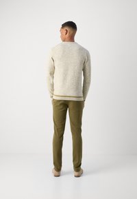 Beige tekstuert genser med ribbestrikket krage og kant, kombinert med grønne slim-fit bukser. Antrekket fullføres med lyse fargede sko.
