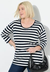 Gestreiftes Oberteil in Marineblau und Weiß mit langen Ärmeln und rundem Ausschnitt, kombiniert mit dunklen Jeans und einer schwarzen Handtasche.