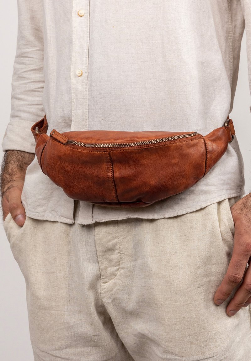 Braune Leder-Bauchtasche mit einer geschwungenen Form und einem Metallreißverschluss. Um die Taille getragen, hat sie eine glatte Textur und minimale Nähte.
