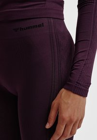 Top atletico viola e leggings presentano un design aderente, texture a coste e dettagli in rete. Il logo "Hummel" è visibile sull'elastico in vita.