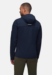 Navy blue insulated jacket with a hood, side panels, and "MAMMUT" logo on the back, featuring smooth texture and durable fabric.