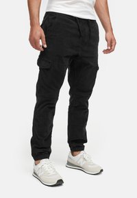 Black cargo pants with a relaxed fit, tapered cuffs, and side pockets; made of soft fabric, paired with white athletic shoes.