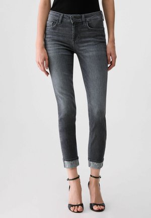 Jeans slim fit grigio scuro con orli risvoltati indossati con top nero senza maniche e tacchi neri aperti con cinturino alla caviglia su una persona.