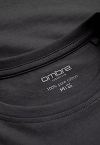 Svart bomulls T-shirt med rundad krage. Taggen visar "ombre bomullsserie," "100% ren bomull," storlek "M" med skötselinstruktioner.