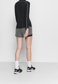 Zwarte langslavige top met witte accenten, gecombineerd met grijze shorts. Model draagt zwarte Nike-schoenen met roze en witte details en witte sokken.