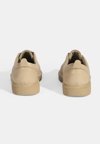 Beige leren schoenen met een afgeronde vorm, lage hak en gestructureerde rubberen zool. De achterkant toont subtiele stiksels en een trekband.