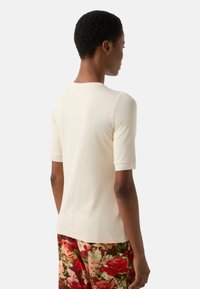 Dopasowany kremowy top z półdługimi rękawami, miękką fakturą, zaokrąglonym dekoltem i widocznymi szwami, zestawiony z kwiatowymi spodniami.