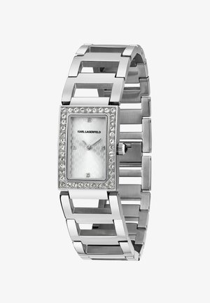 Silberne rechteckige Uhr mit strukturiertem weißem Zifferblatt, umgeben von einer Kristall-Lünette und einem klobigen Gliederarmband-Design.