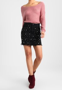 Rosa texturerad stickad tröja med off-shoulder-design, kombinerad med en svart denim mini-kjol prydd med vita nitar och fransad fåll. Röda ankelstövlar.